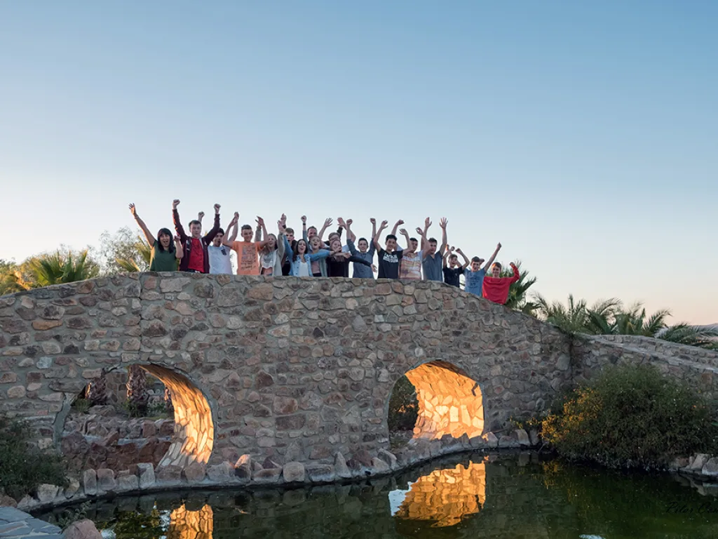 Die Gruppe steht mit erhobenen Armen auf einer alten Steinbrücke über dem Wasser.